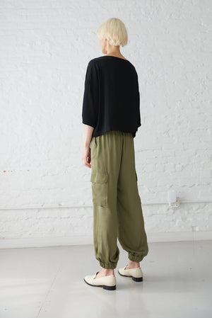 woman wearing satin boatneck top made from sustainable viscose in black and olive jogger pants back view