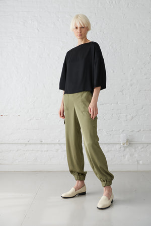 woman wearing satin boatneck top made from sustainable viscose in black and olive jogger pants