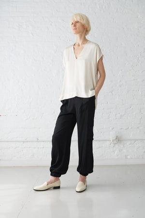 woman wearing tie neck blouse made with a luminous polished viscose satin in ivory and black jogger pants front view